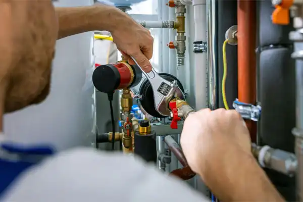 Person using a wrench to adjust plumbing pipes and connections in a mechanical room.