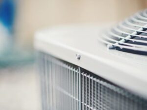 Close-up of an outdoor air conditioning unit with visible metal grating and a fan on top.