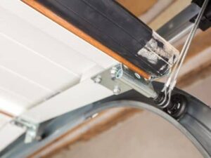 Close-up of a garage door track mechanism with a cable and roller system, showing metal brackets and white panels.