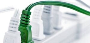 Close-up of a row of electrical plugs in a power strip, with one green plug among several white ones.