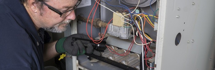 HVAC Technician looking in furnace with flashlight